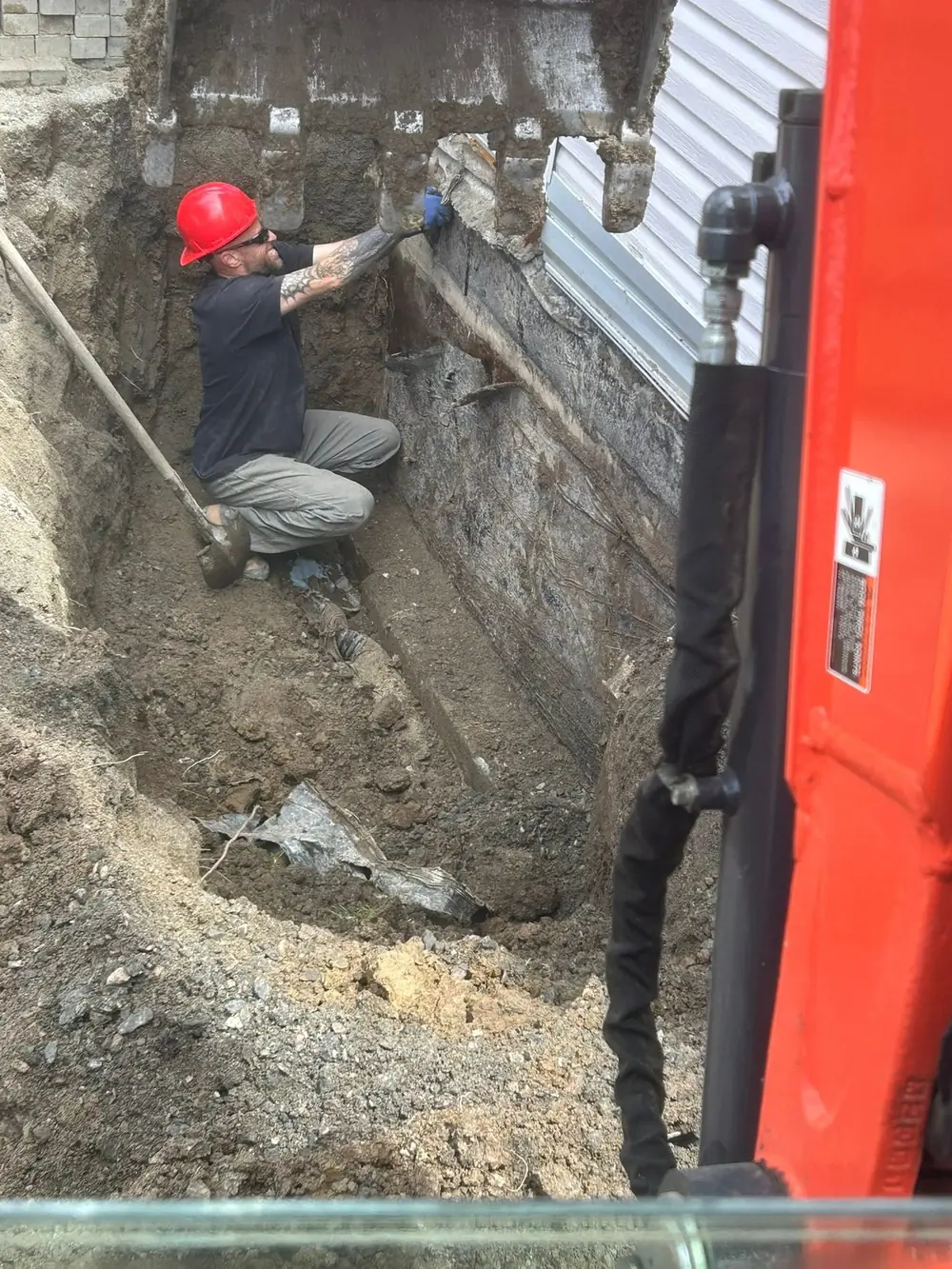 LKC Foundations crew member working in deep excavation against an exterior basement foundation wall