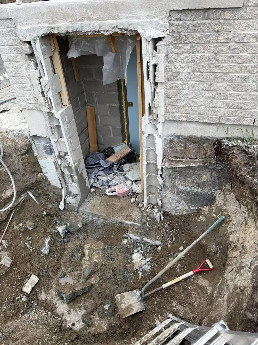 New basement entrance opening built from the exterior with fresh concrete block and excavated trench